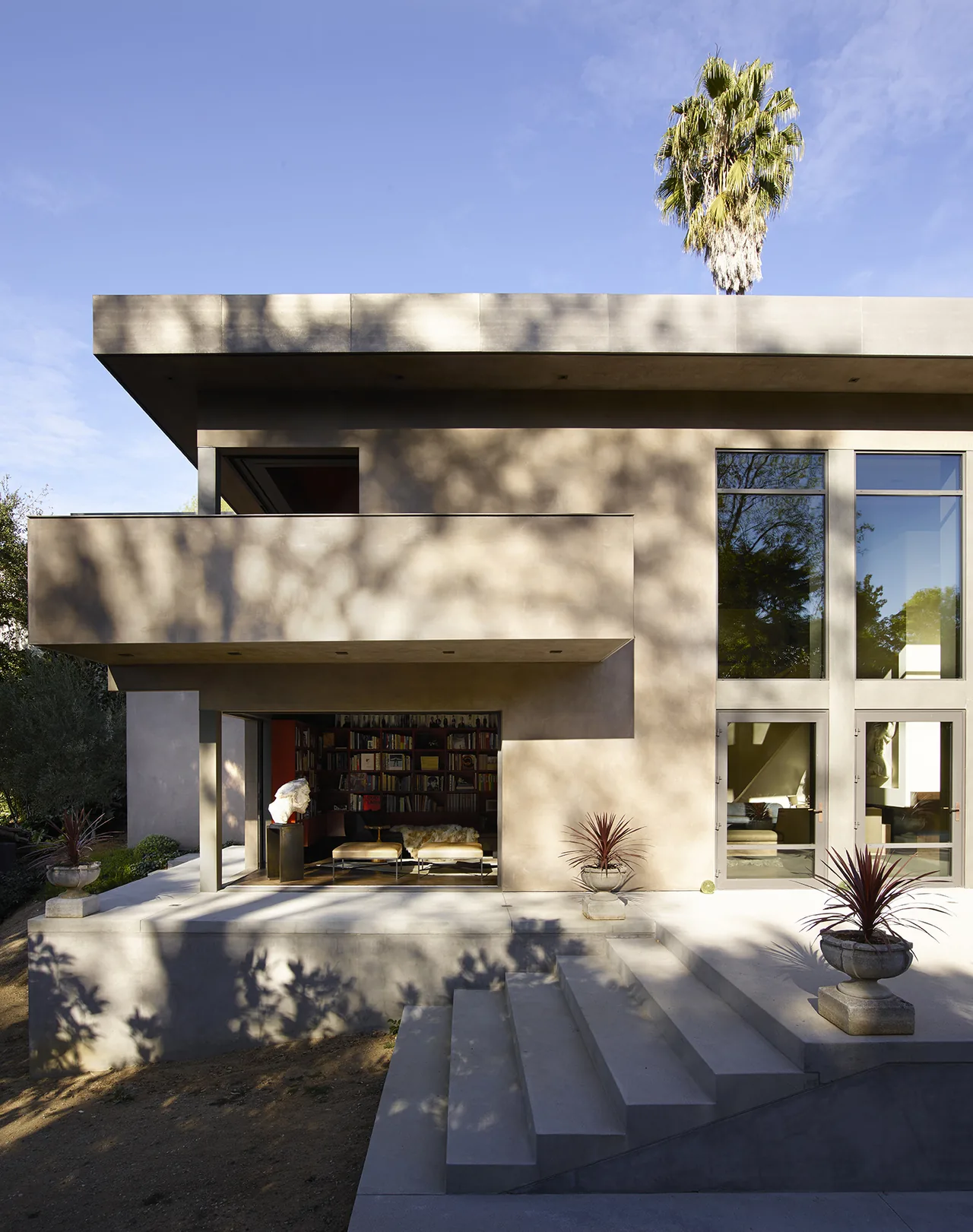 Modern house exterior with large windows, cantilevered balcony, and concrete steps at Hollywood Hills House by CHU+GOODING Architects.