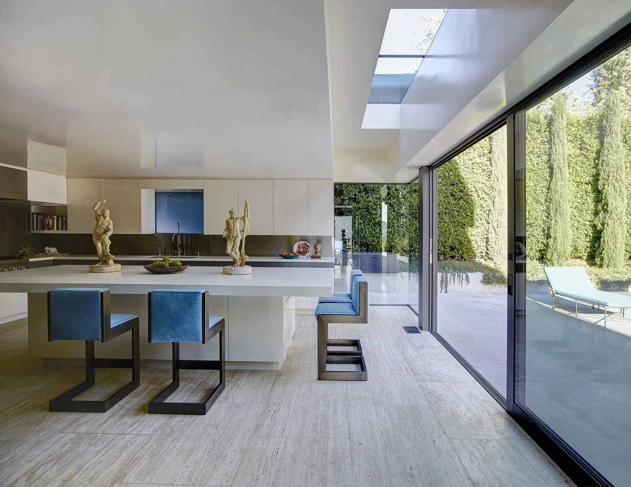 Kitchen features a large white island with sculptural decor, blue bar stools, and expansive sliding glass doors to the outdoor patio.