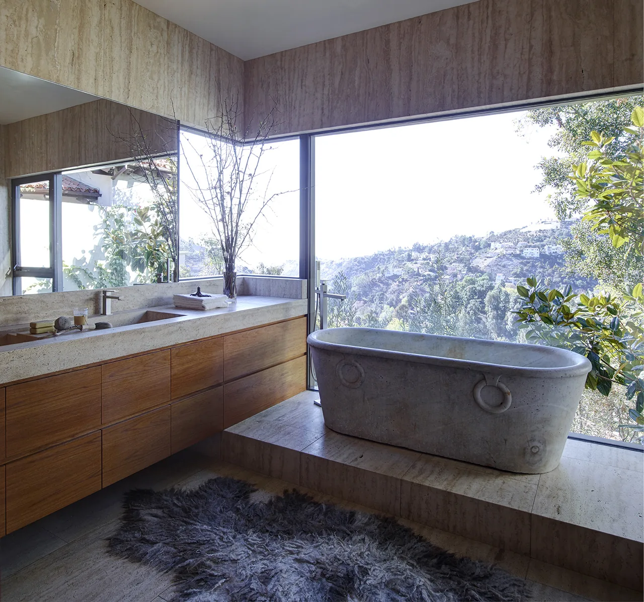 Stone freestanding tub with large window overlooks hillside in this bathroom.