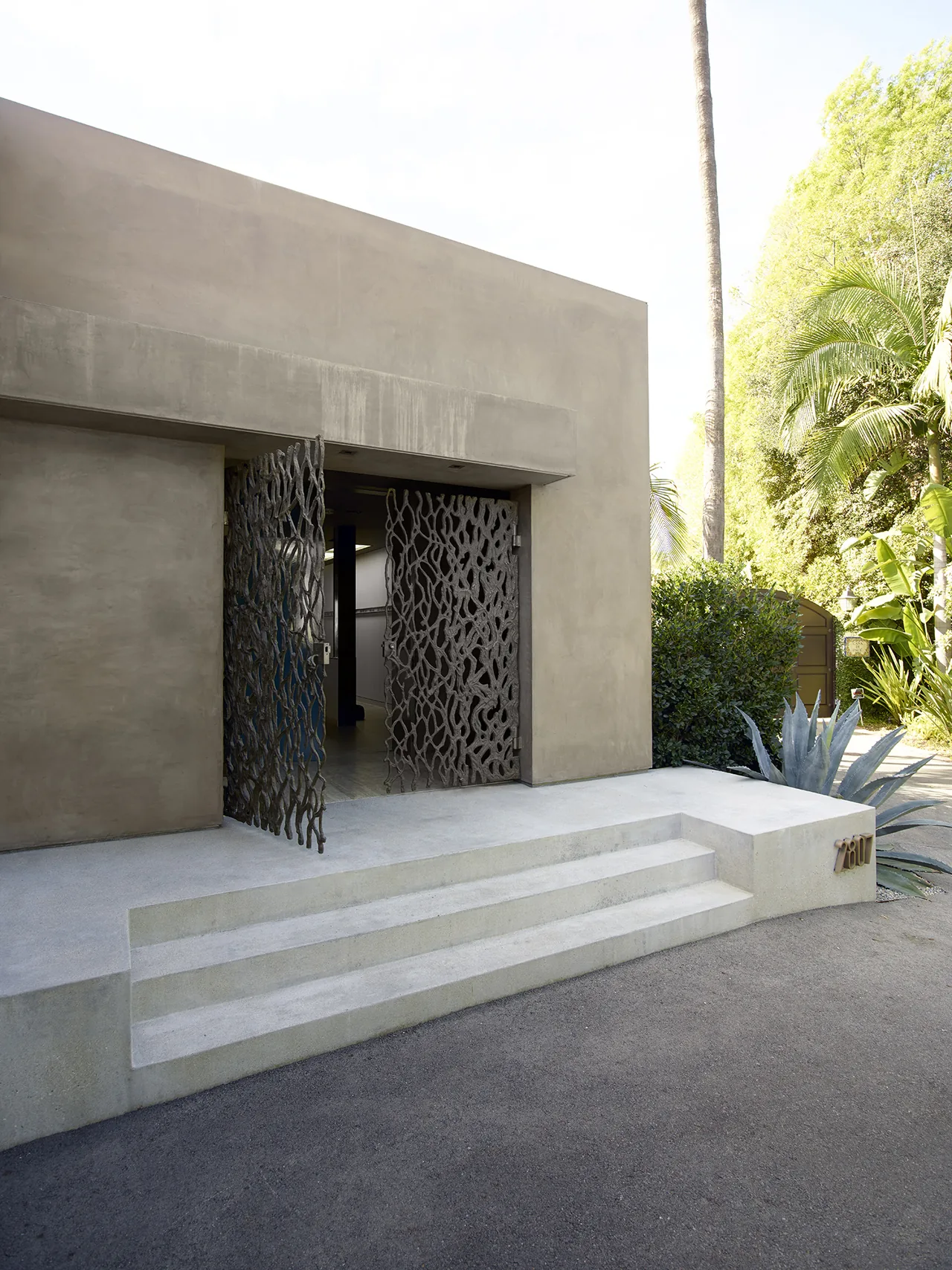 The Hollywood Hills House features a minimalist exterior with artistic metal front doors and smooth concrete steps.