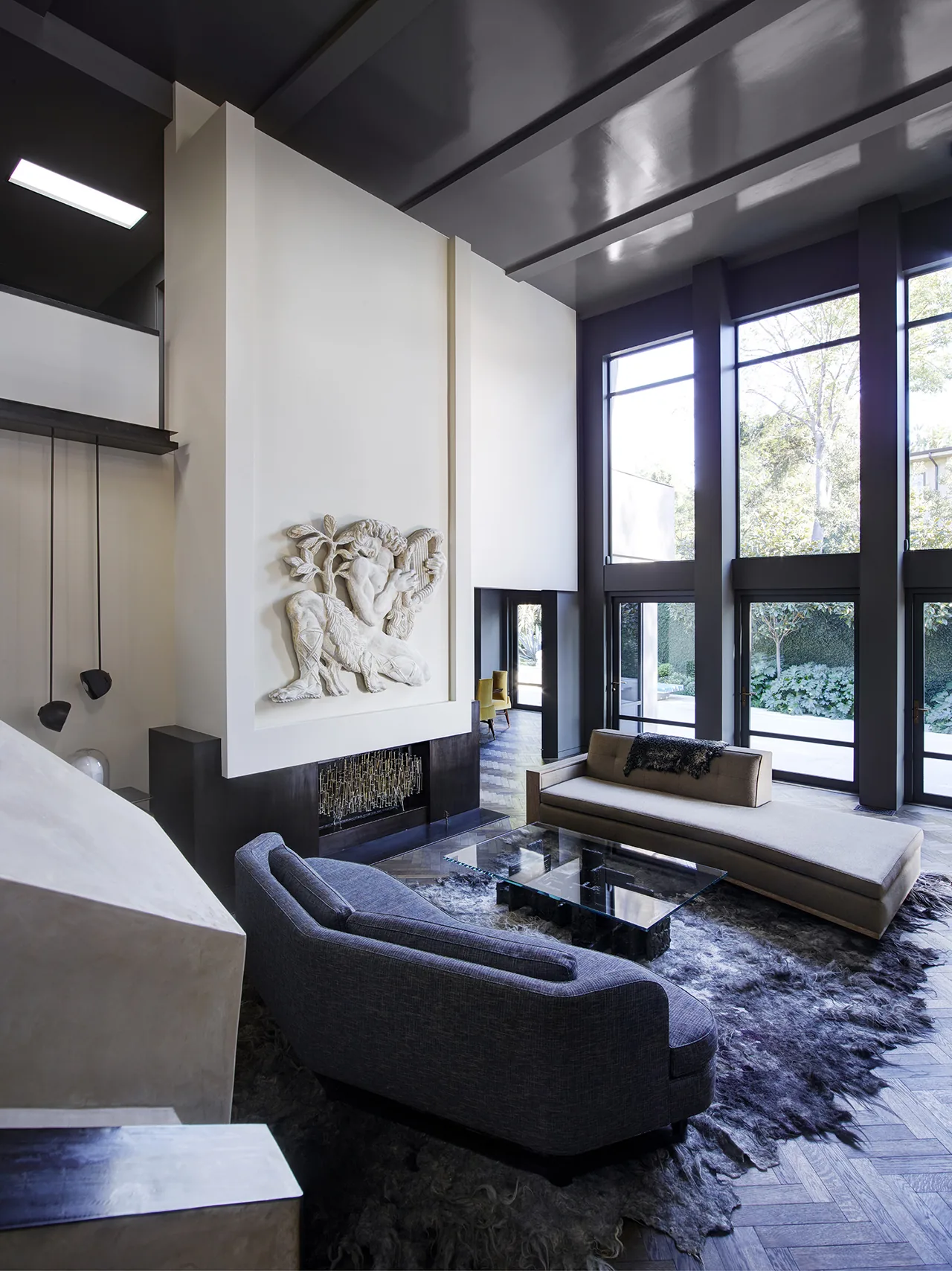 Living room of Hollywood Hills House features large windows, sculptural wall relief, and modern furnishings by CHU+GOODING Architects.