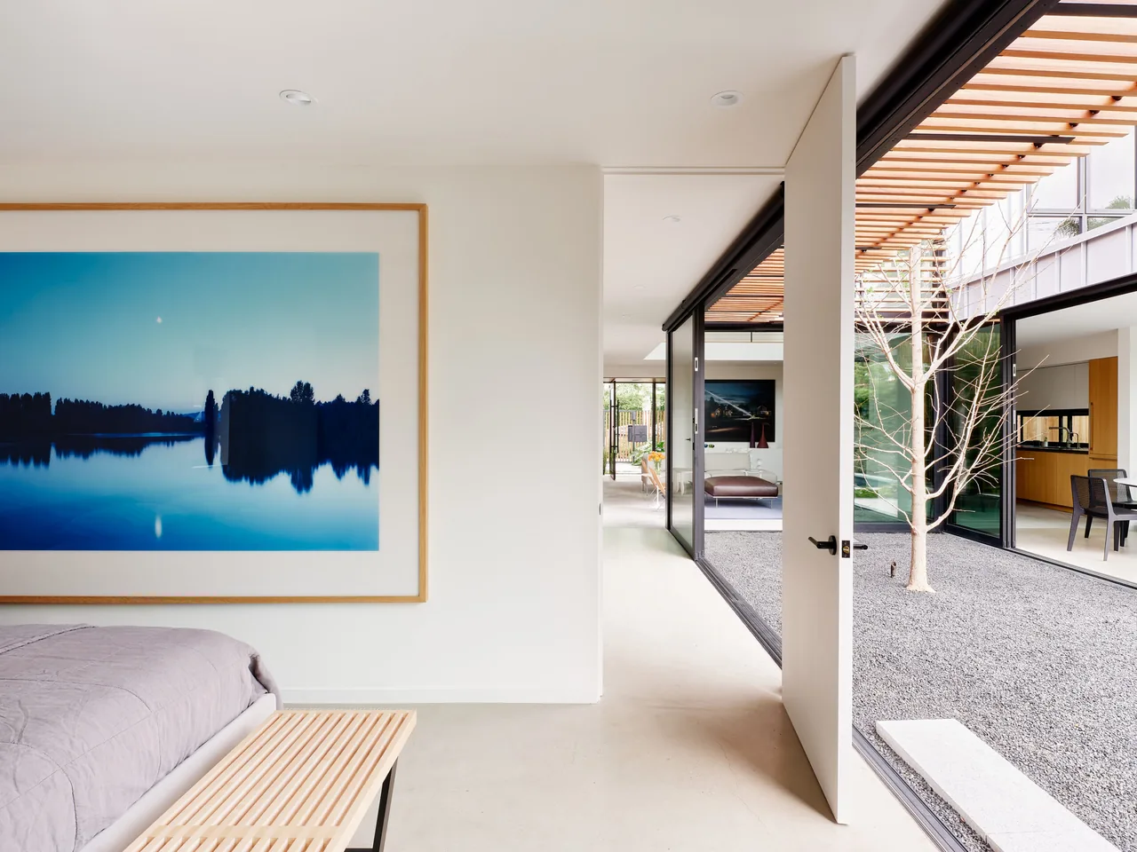 This Los Angeles residence features a bedroom opening onto a minimalist gravel courtyard with a single tree, framed by black sliding doors.