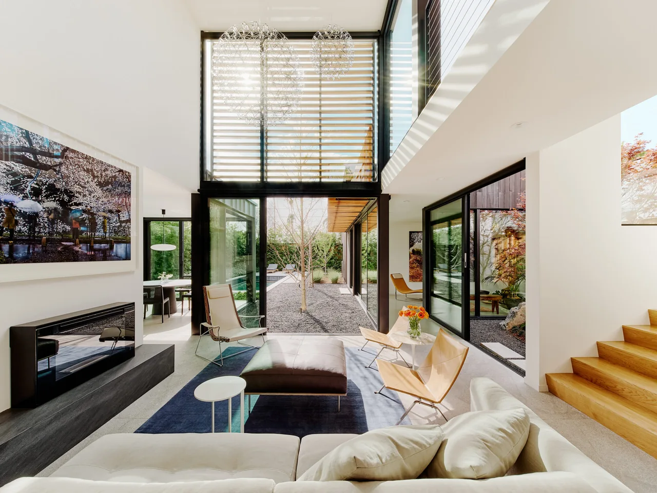 Living room with floor-to-ceiling black-framed windows and sliding glass doors opening to a landscaped courtyard.