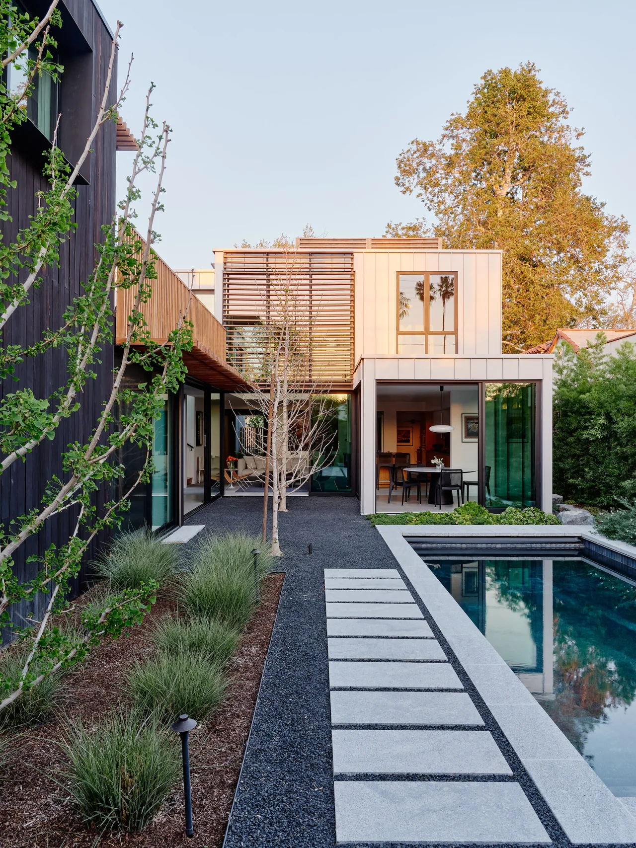 Backyard view of a Los Angeles residence featuring a pool, gravel pathway, slatted wood privacy screens, and floor-to-ceiling glass doors.