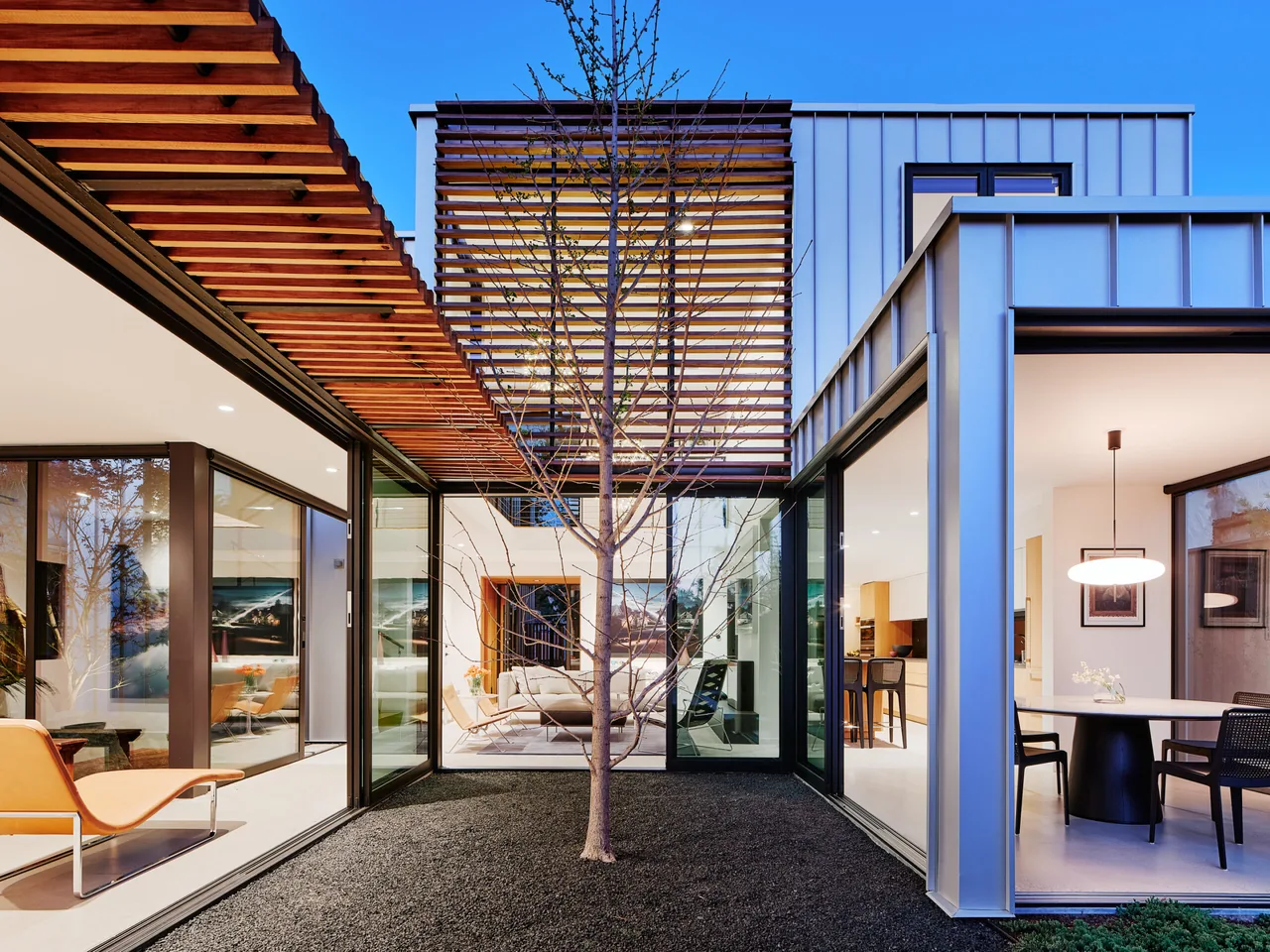 Modern Los Angeles residence features a central gravel courtyard with a leafless tree and wood slat ceiling beams.