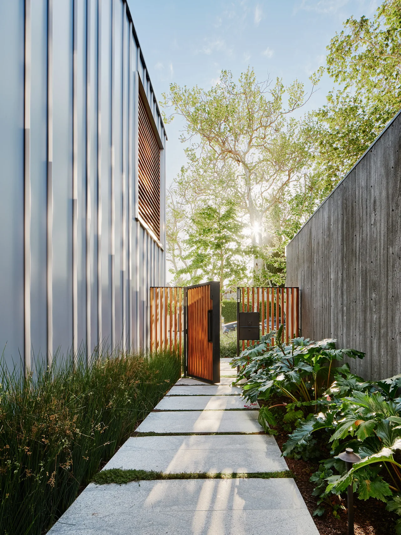 Pathway entrance with a wooden gate between metal siding and a concrete wall at a Los Angeles residence.