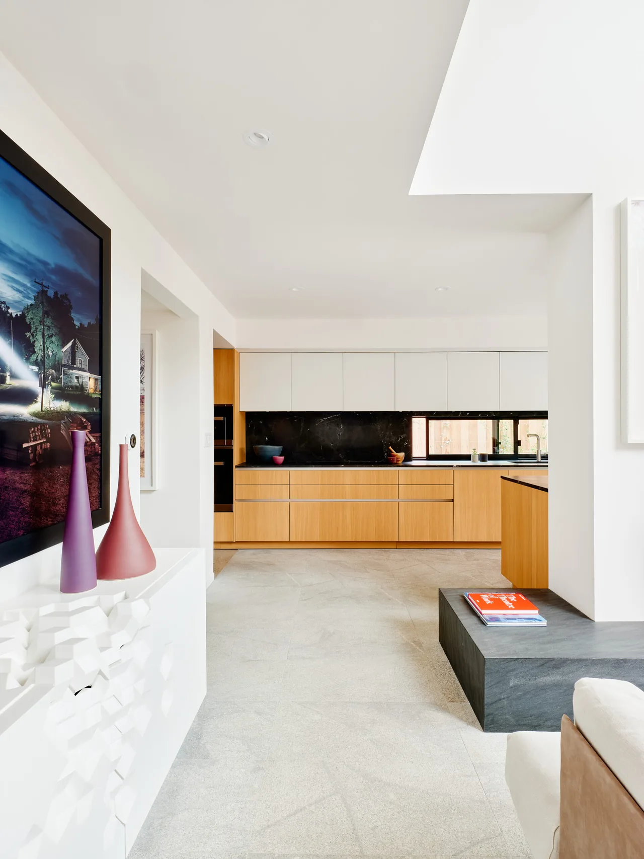 Kitchen with light wood and white cabinets, black stone backsplash, and a horizontal window overlooking the exterior.