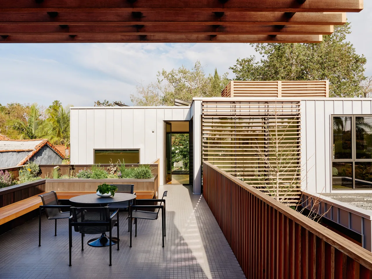 Patio with wood-paneled ceiling and black mesh chairs at the Los Angeles residence by Clive Wilkinson Architects.