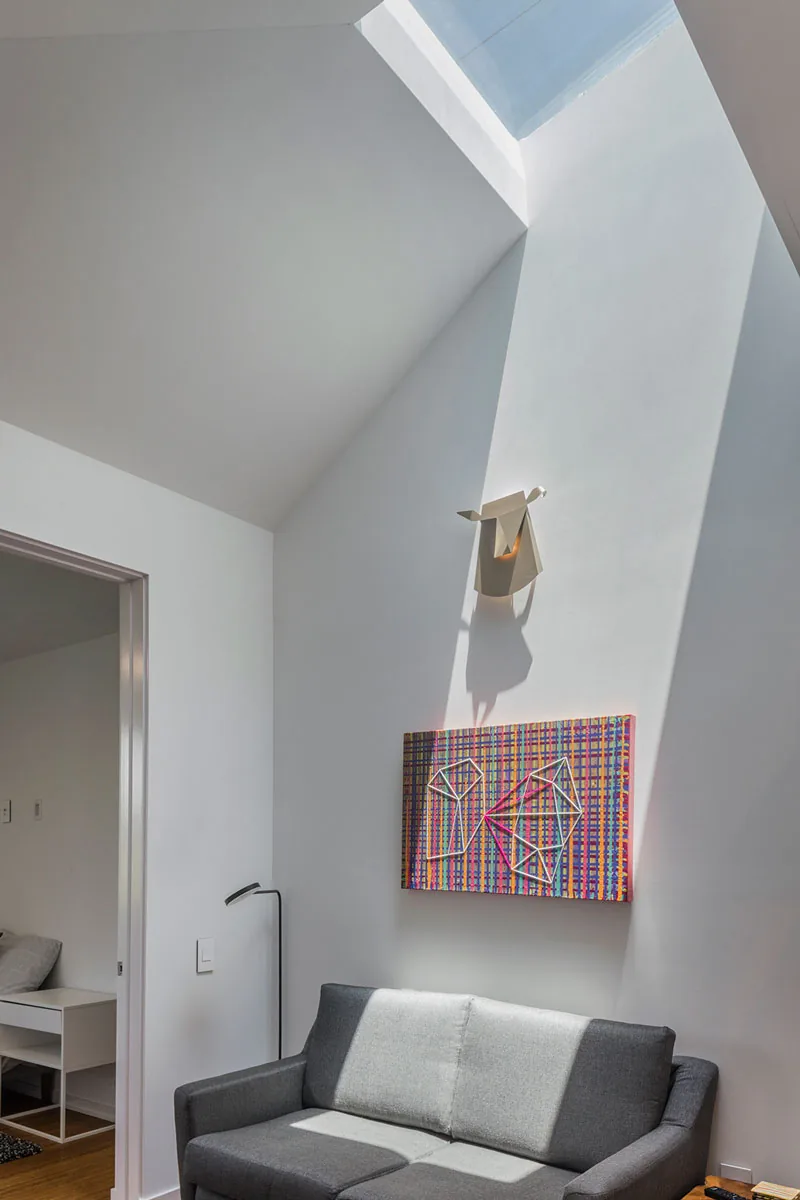 Living space in HOUSE 2344 features a skylight, gray sofa, and abstract wall art enhancing natural light.