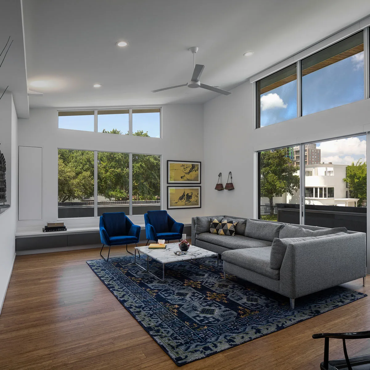 Living room in HOUSE 2344 features floor-to-ceiling glazing and modern furnishings with blue accent chairs and art on walls.