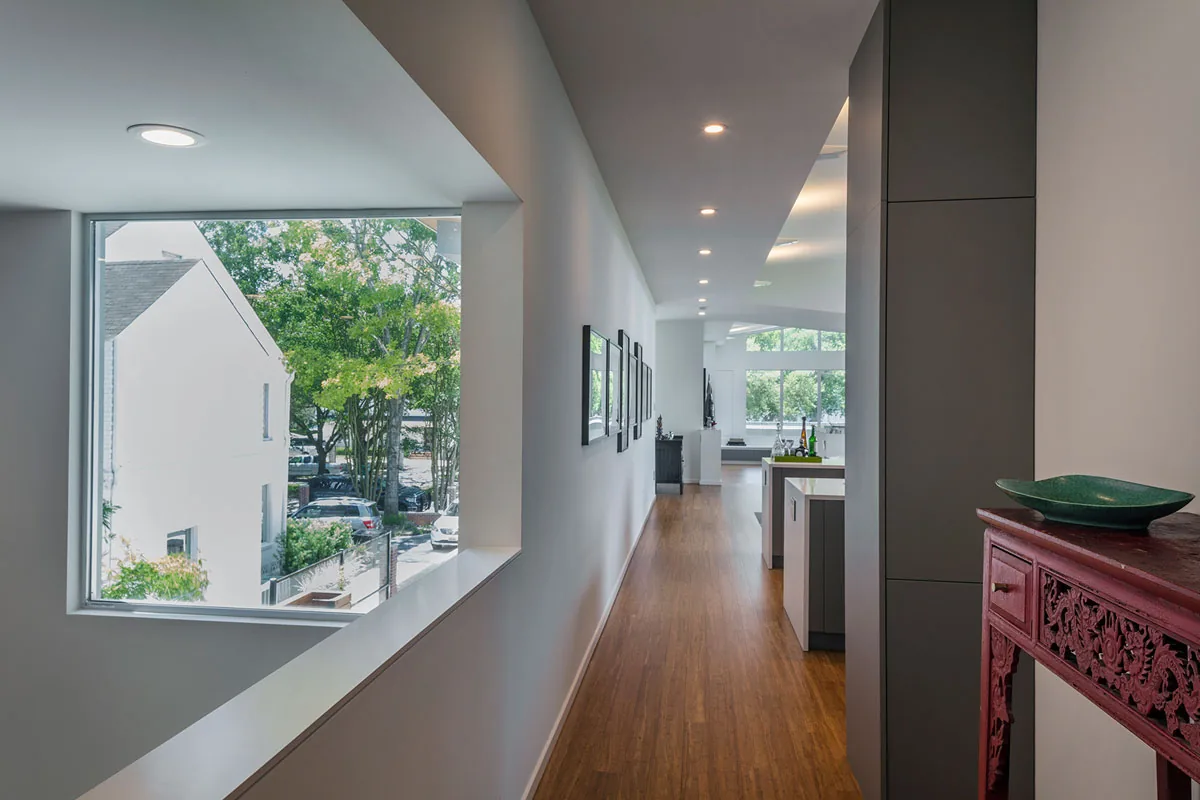 Interior hallway with wood flooring and a large window offering views of neighboring house and trees.