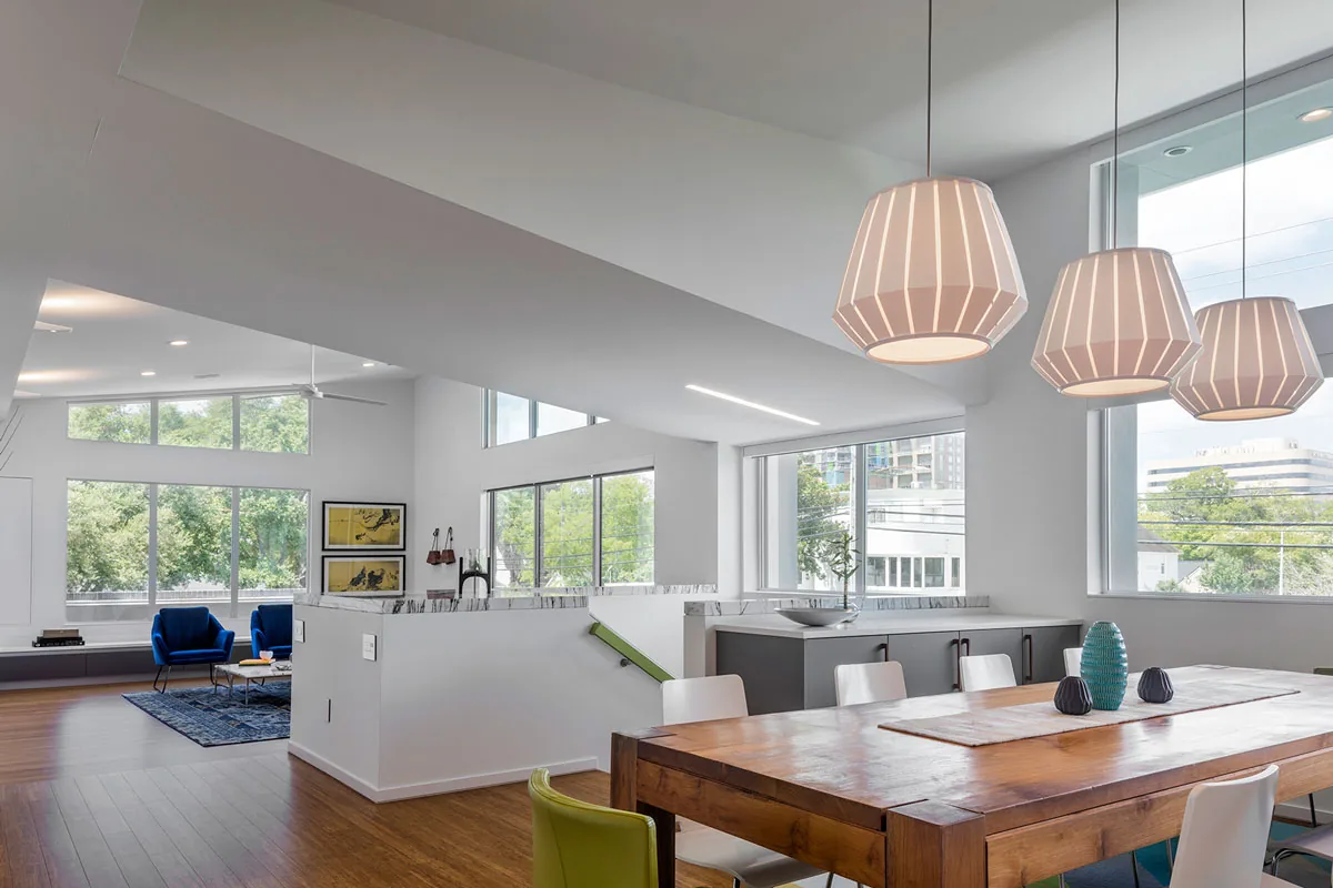The open interior features a wood dining table, blue armchairs, and large windows providing expansive natural light.