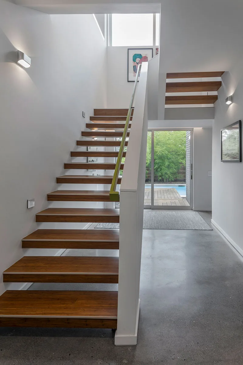 Modern interior with floating wooden stairs and concrete floor opens to sliding glass door and outdoor greenery.