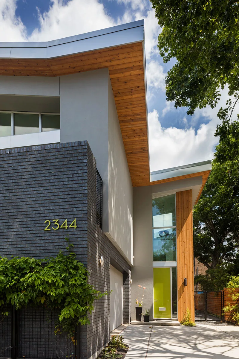 HOUSE 2344 features a modern exterior with gray brick, wood siding accents, and a green entrance door beneath angled rooflines.