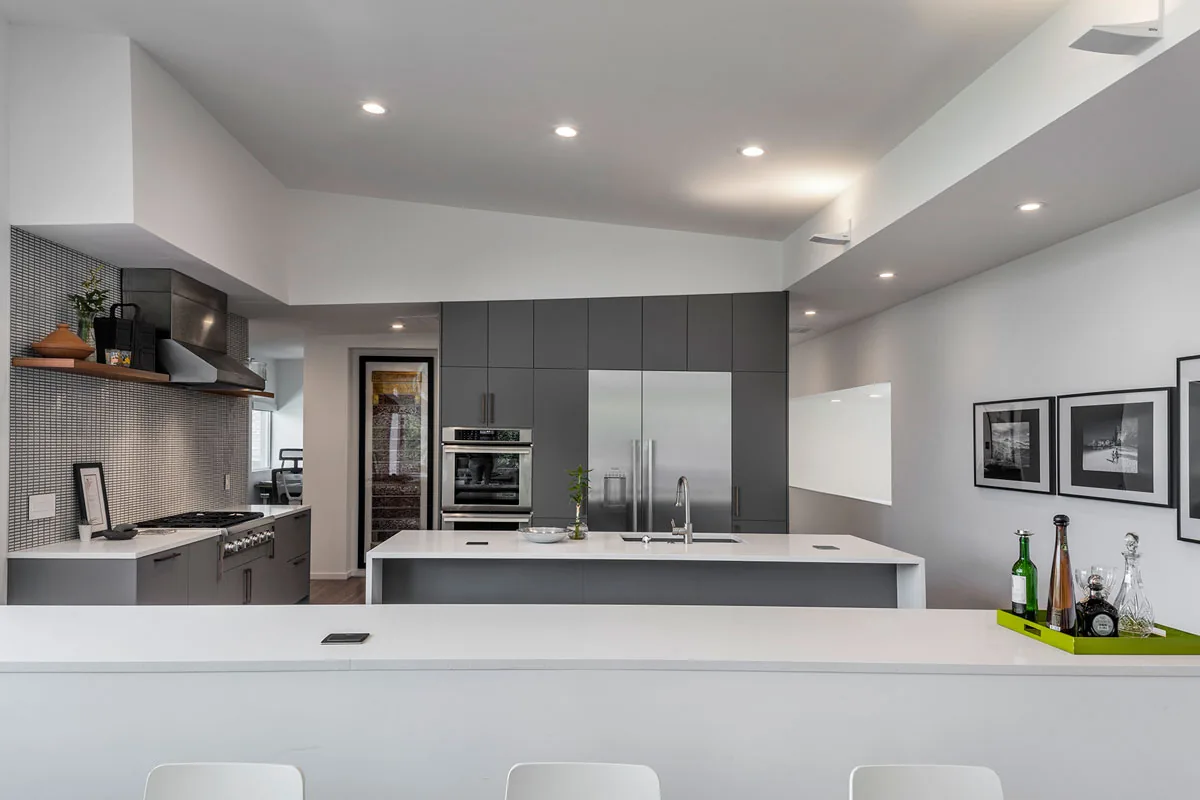 Kitchen features gray cabinets, a central island with sink, and stainless steel refrigerator and oven.
