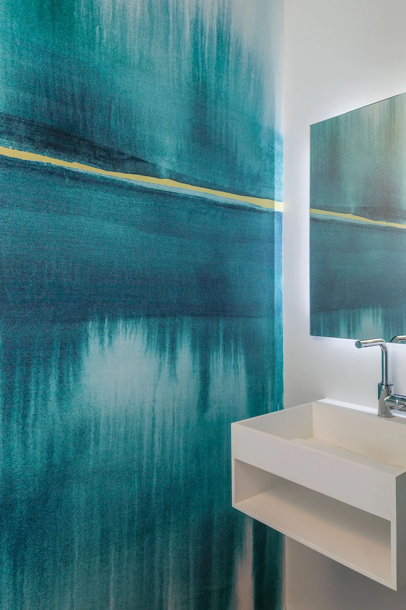A white wall-mounted sink contrasts with bold teal wall art in this modern bathroom.