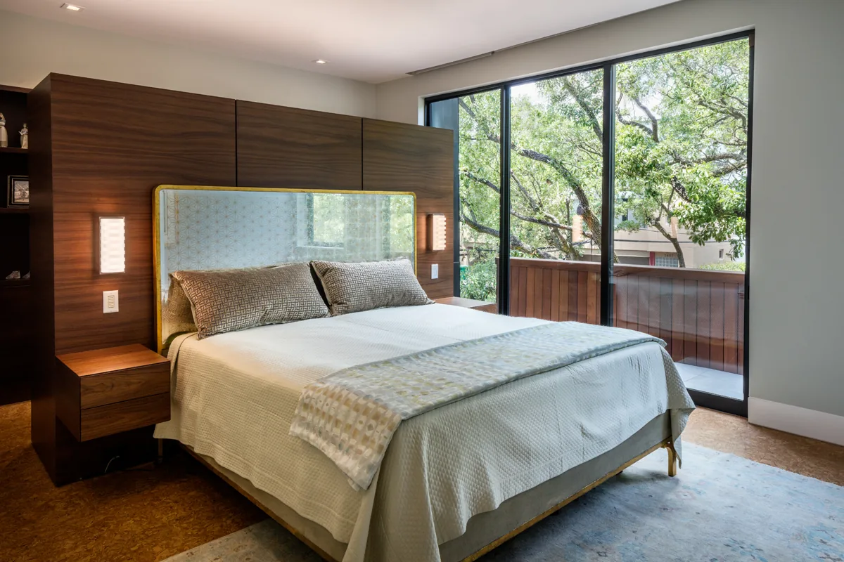 Bedroom features a wooden headboard wall, bedside lighting, and large glass sliding doors opening to a balcony.
