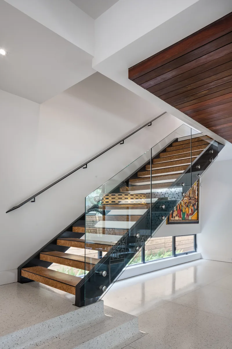 Interior staircase with glass railing and wooden treads in a modern home with terrazzo flooring.