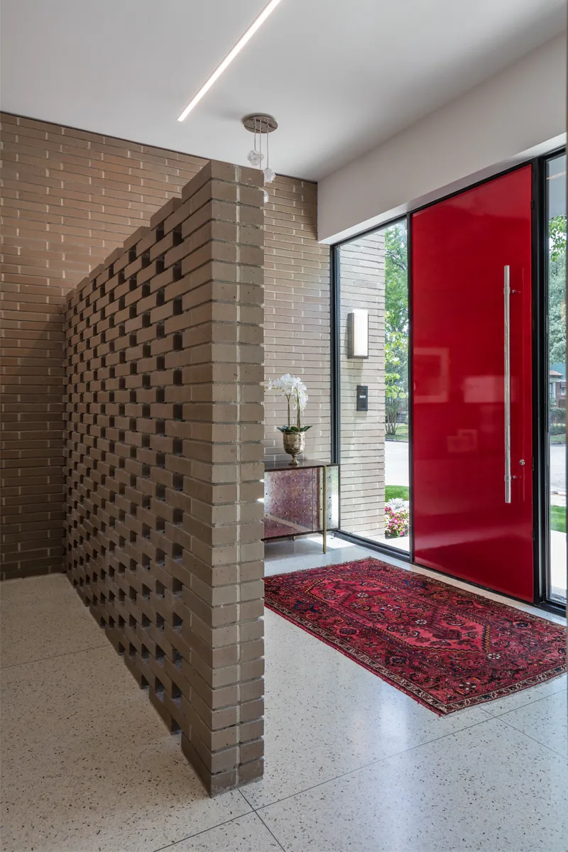 Entry showcasing a red pivot front door, open brick partition, and terrazzo floor in HOUSE 1700 by Collaborative Design Works.