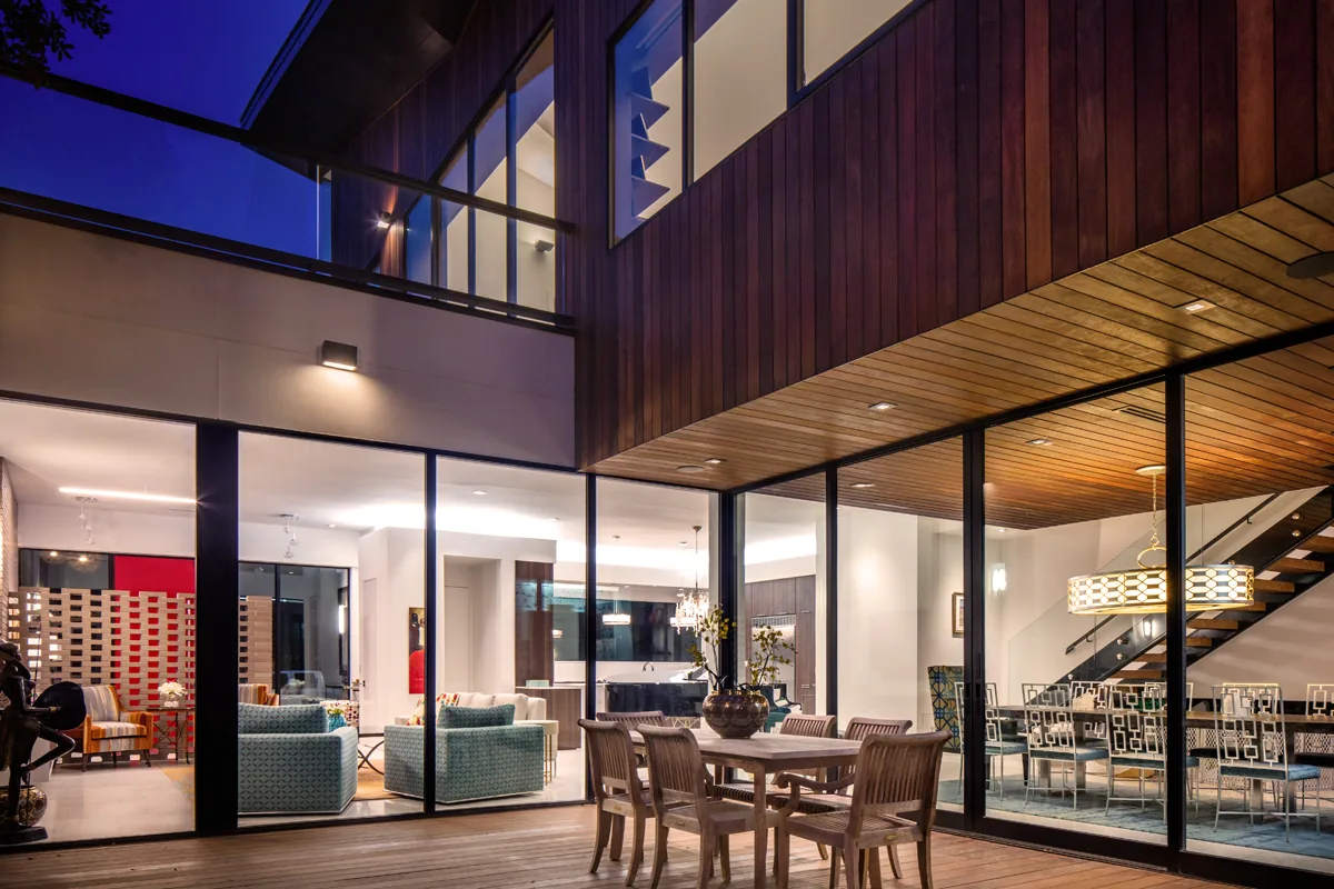 HOUSE 1700 features an outdoor dining area with wooden furniture beneath a wood-paneled ceiling and large glass walls.