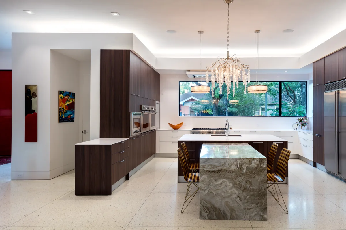 Kitchen with marble island, dark wood cabinets, large horizontal window, and two pendant lights inside modern home.