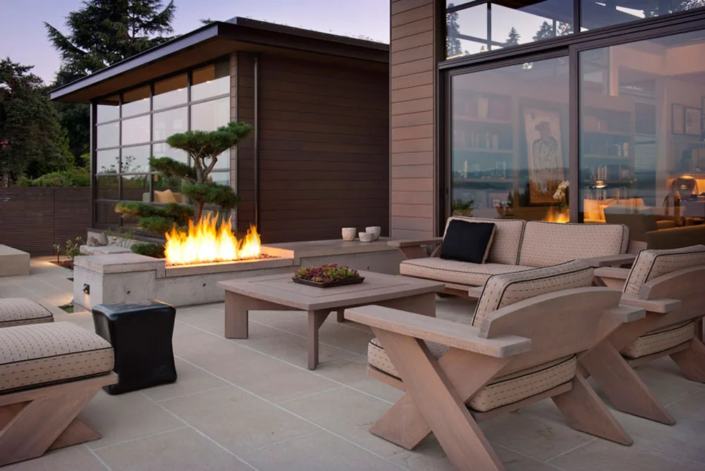 Outdoor living patio includes cushioned seating and a concrete fire feature near the Washington Park Residence by Conard Romano Architects.