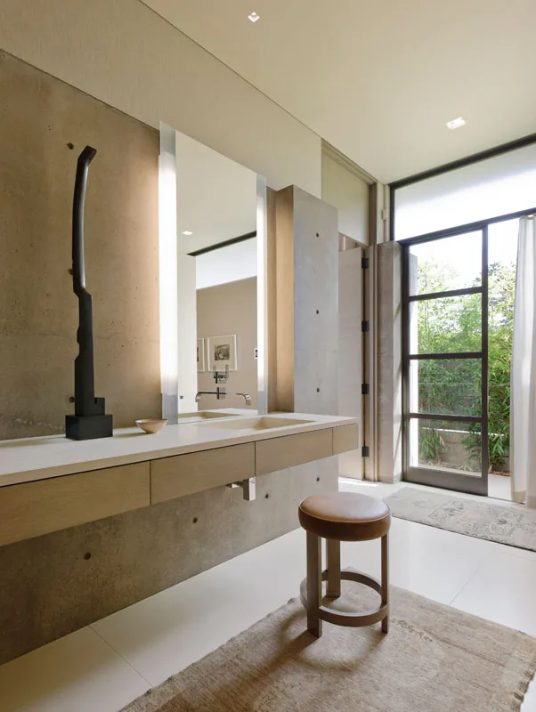 Bathroom features concrete walls, a floating wood vanity with dual sinks, and a large multi-pane window door providing natural light.