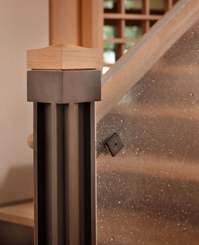 A metal and wood newel post supports a glass balustrade on the stair of the Engawa House in Seattle.