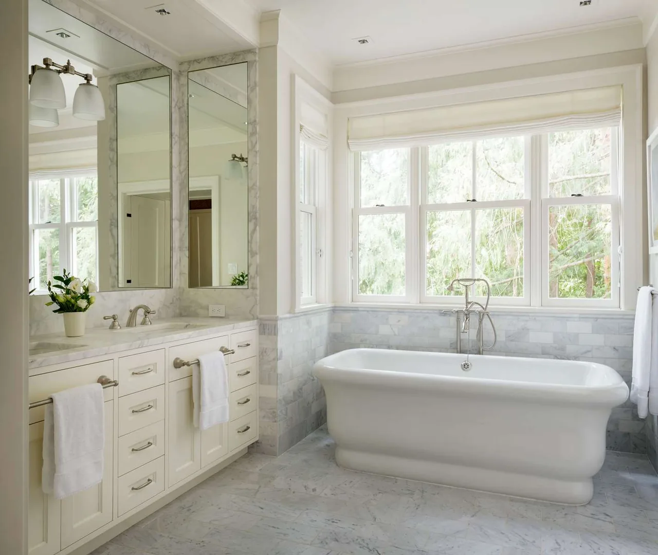 This modern farmhouse bathroom by Conard Romano Architects includes a freestanding tub and a double-sink vanity with marble surfaces.