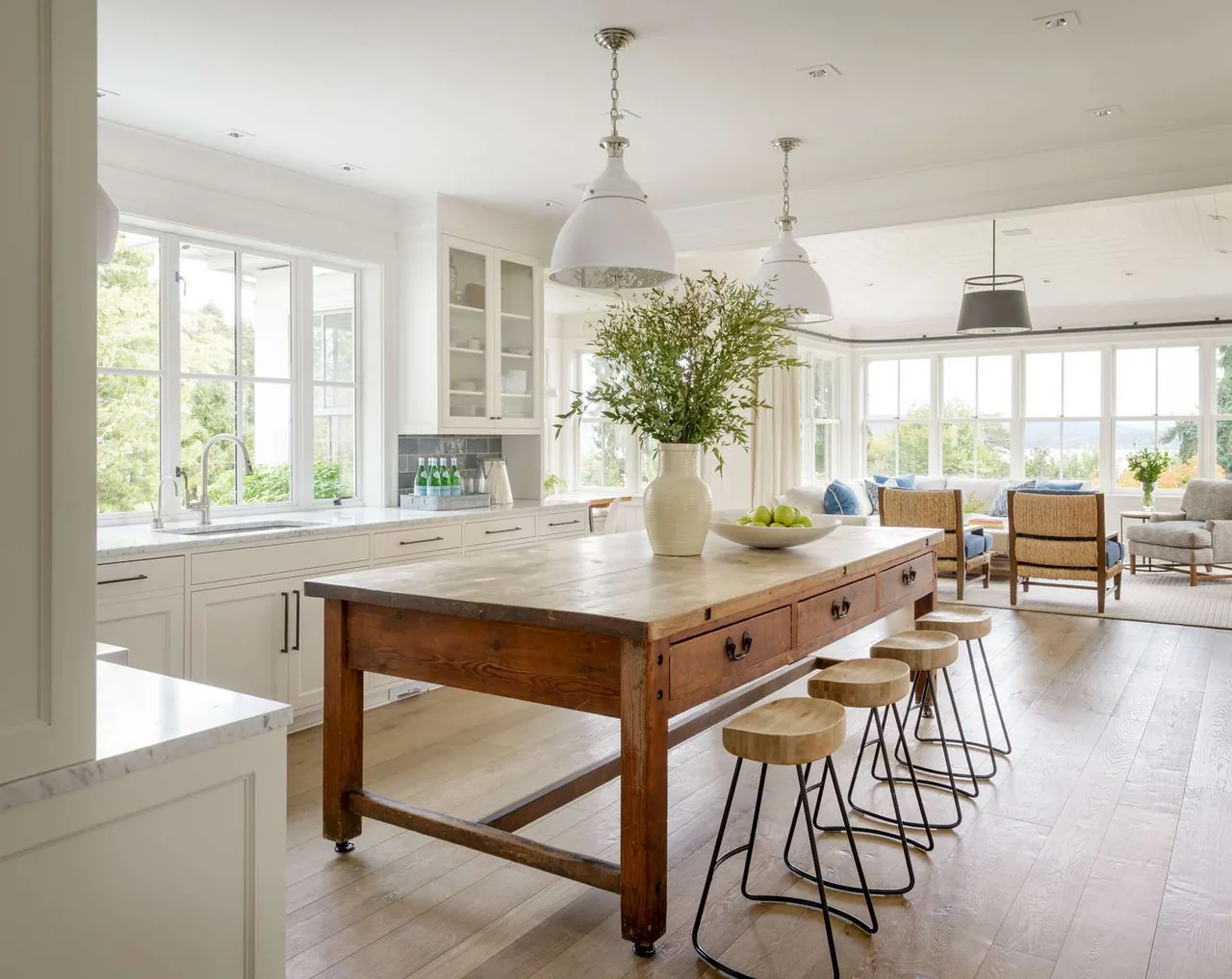 Modern farmhouse kitchen with a wooden island and adjoining living room featuring large windows and natural light.