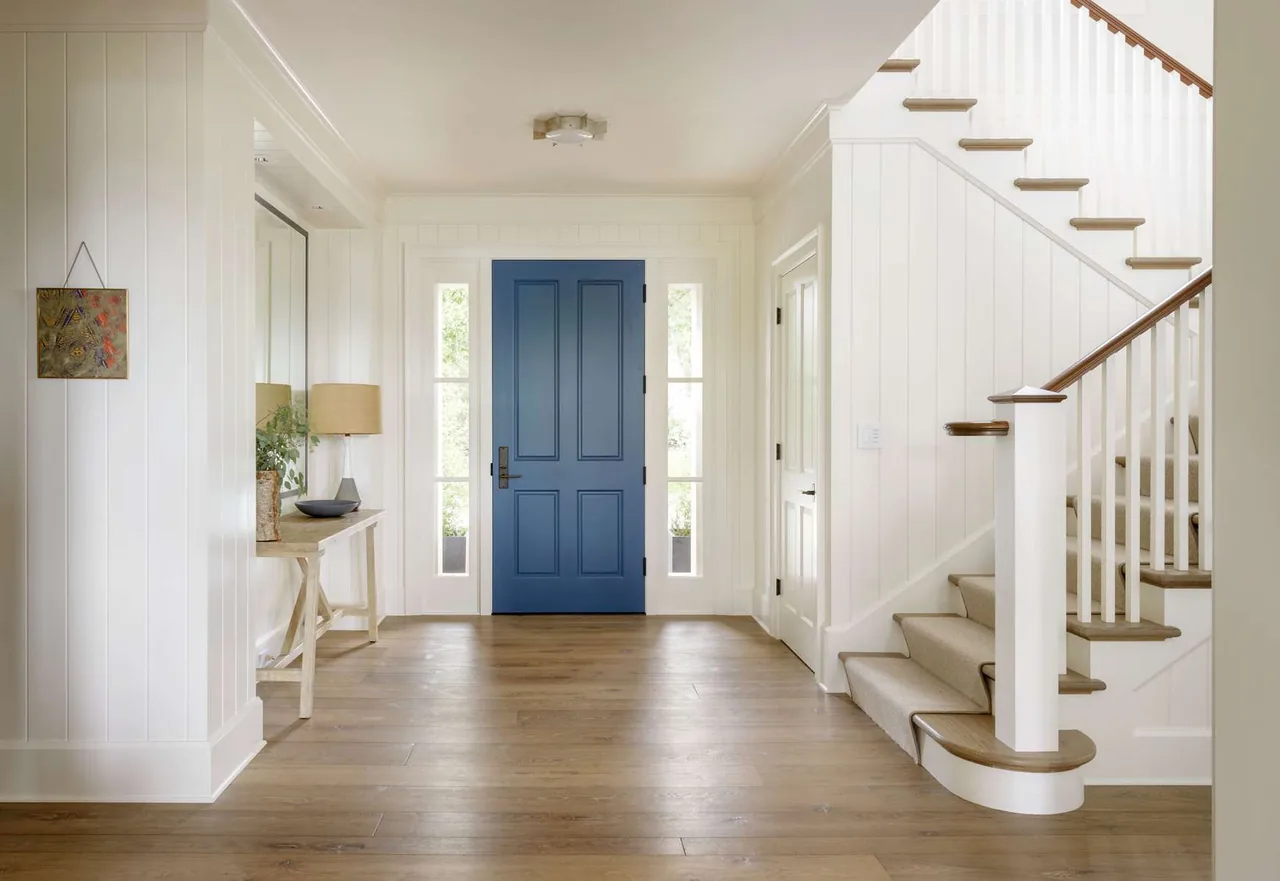 Entryway features a blue front door flanked by narrow windows and a staircase with wood handrail and white balusters.