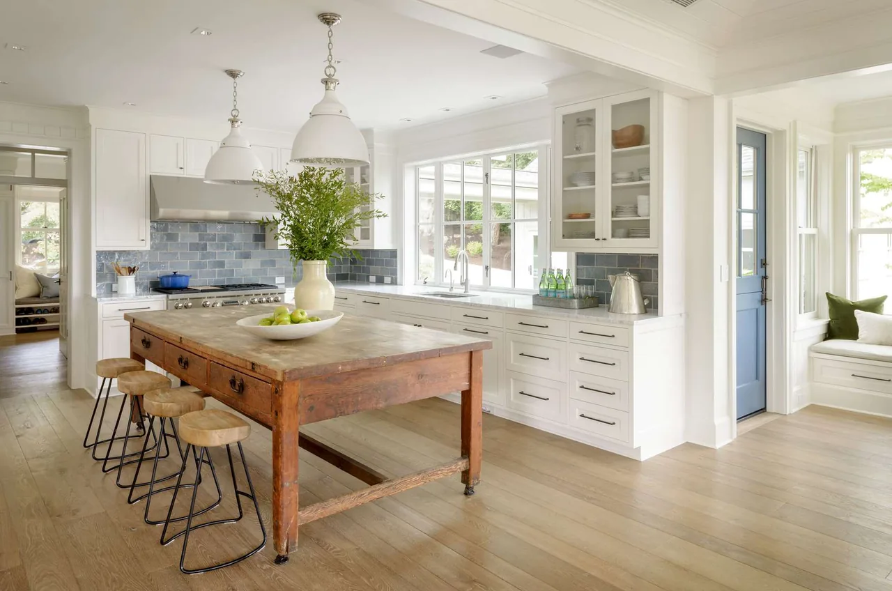 Modern farmhouse kitchen with a large wooden island, white cabinets, and light hardwood floors, featuring a blue door and blue tile backsplash.