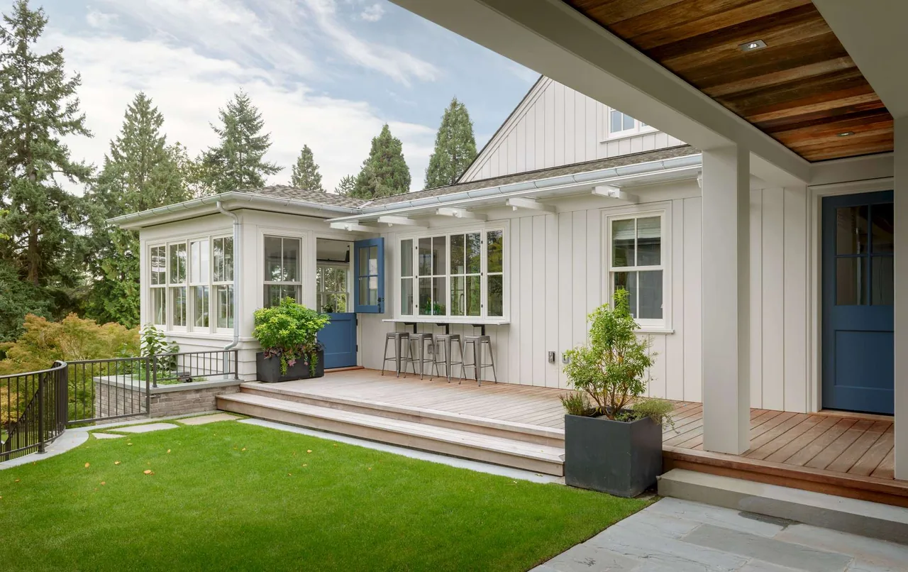 Modern farmhouse exterior with vertical siding, a covered porch, and blue doors opening onto a wooden deck.