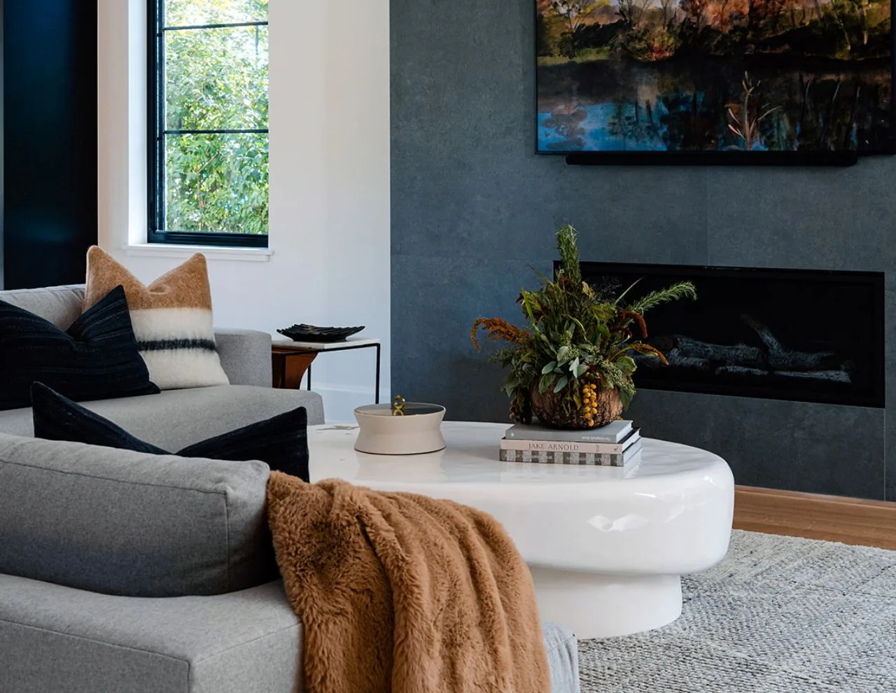 Living room with gray upholstered sofas, a white coffee table with a floral centerpiece, and a modern gas fireplace.