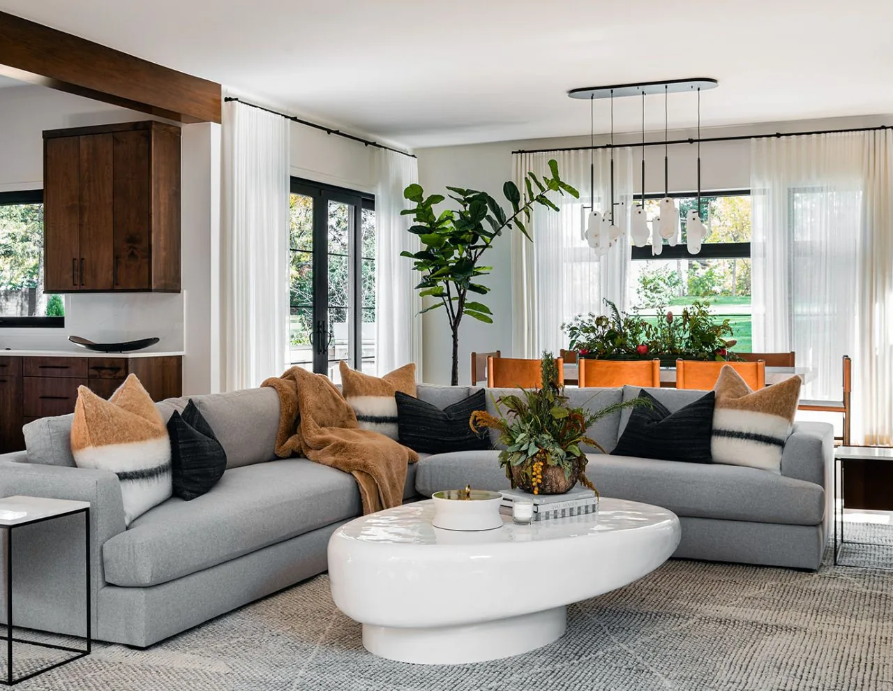 Living room with a light gray sectional sofa, decorative pillows, and a sculptural pendant light above the white coffee table.