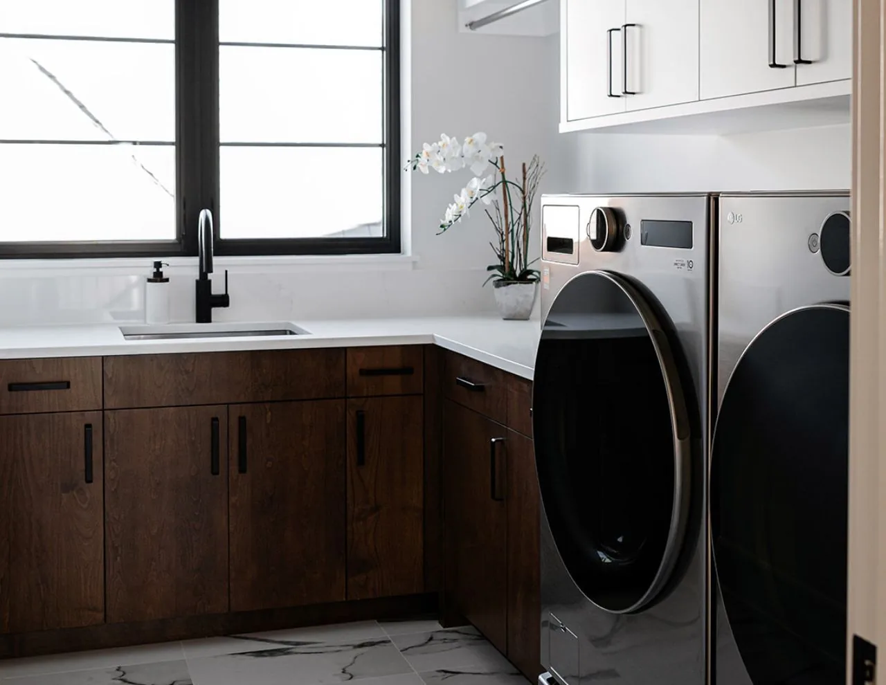 Laundry room at Clarendon Hills Residence with dark wood cabinetry and modern stainless steel washer and dryer units.