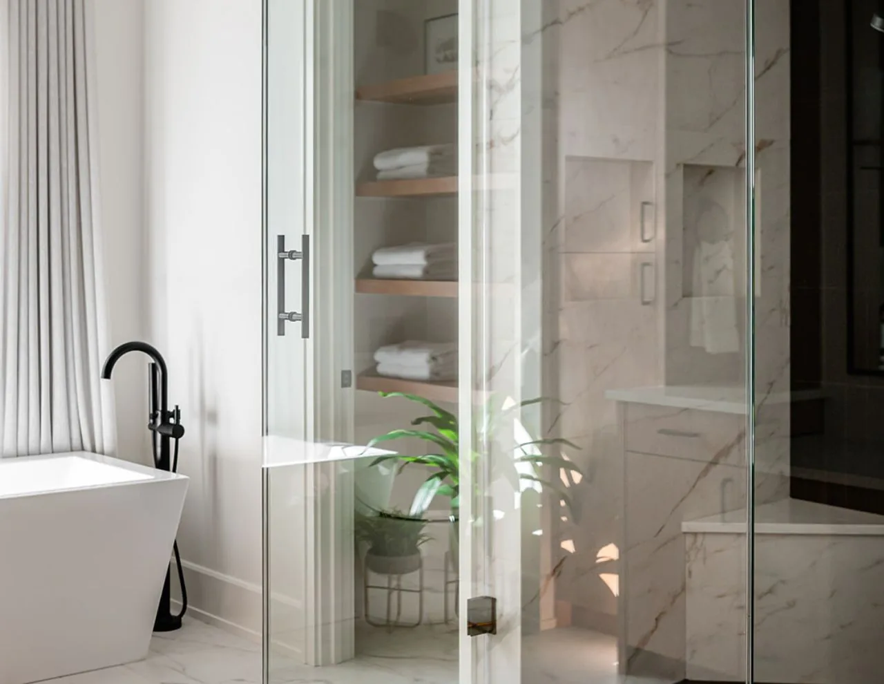 Bathroom features a white freestanding tub, black floor-mounted faucet, glass shower door, marble-look tile, and wood shelves with folded towels.