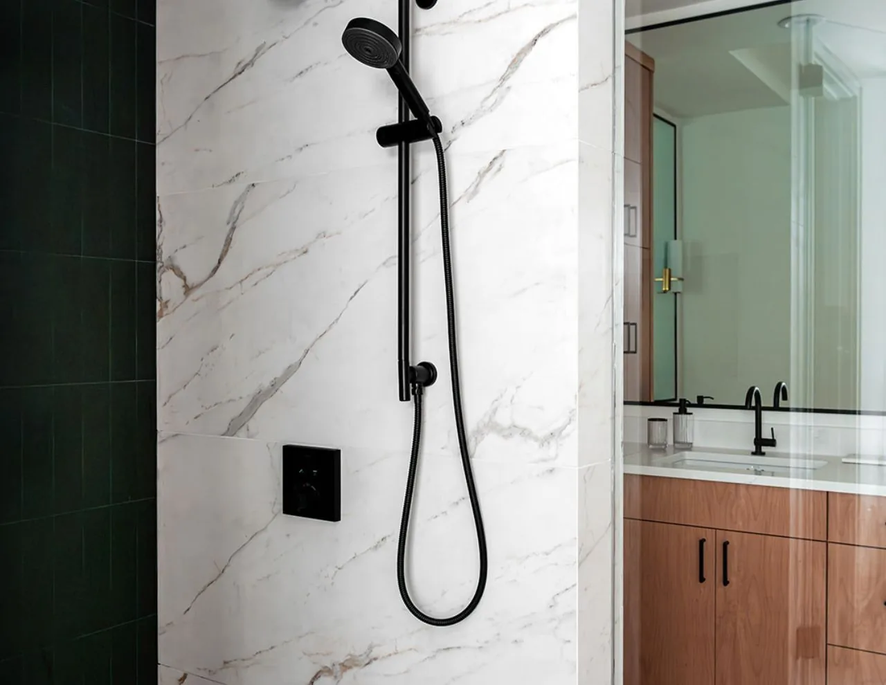 A bathroom shower features a black matte handheld showerhead on a white marble tile wall.