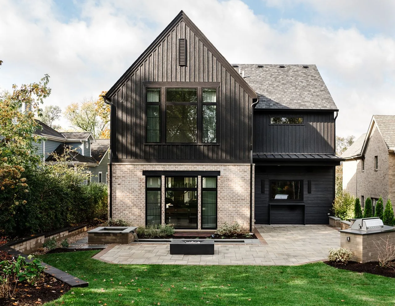 Clarendon Hills Residence with contrasting black wood siding and white brick, featuring large black window frames and a paved patio area.