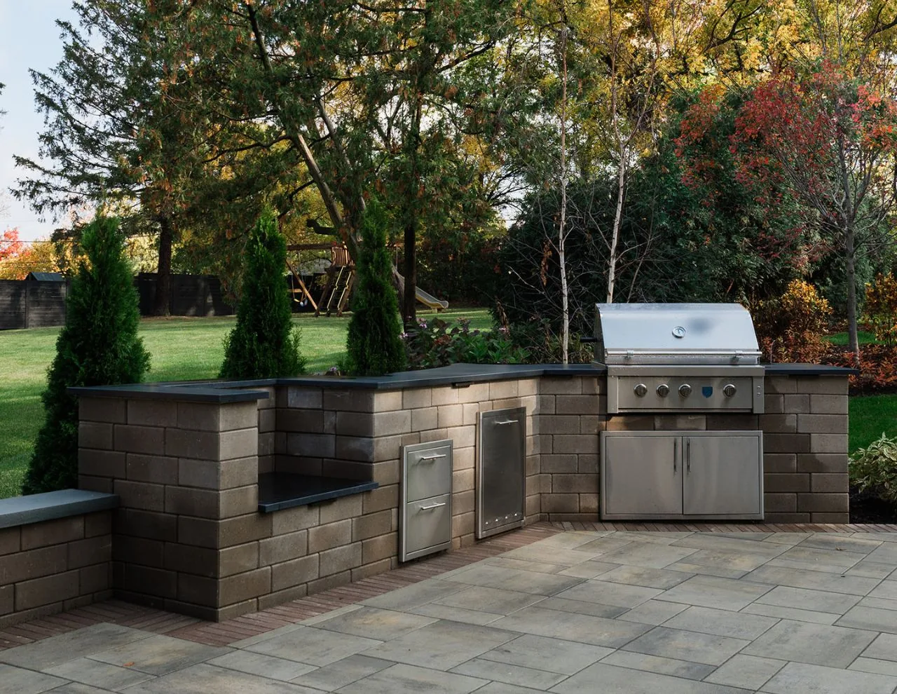 Clarendon Hills Residence features an outdoor kitchen with a built-in grill and stone counter walls on a spacious patio.