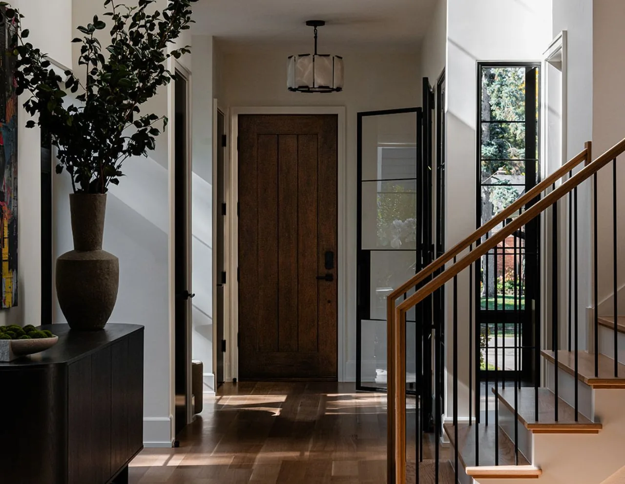 Entry hallway features a solid wood front door, black-framed windows, and wood stairs with metal balusters.