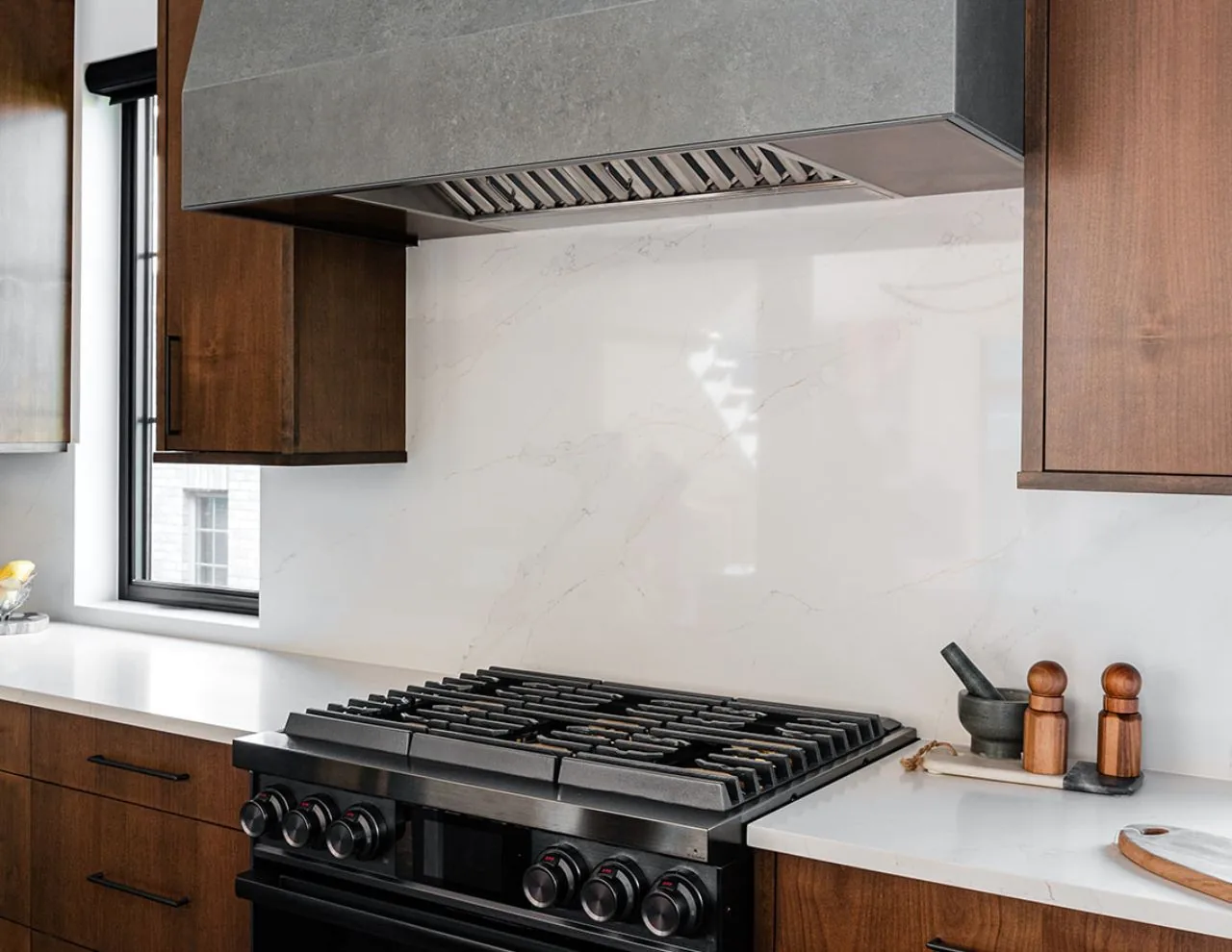 Kitchen cooking area featuring a gas range with stainless steel hood and wood cabinetry in the Clarendon Hills Residence.