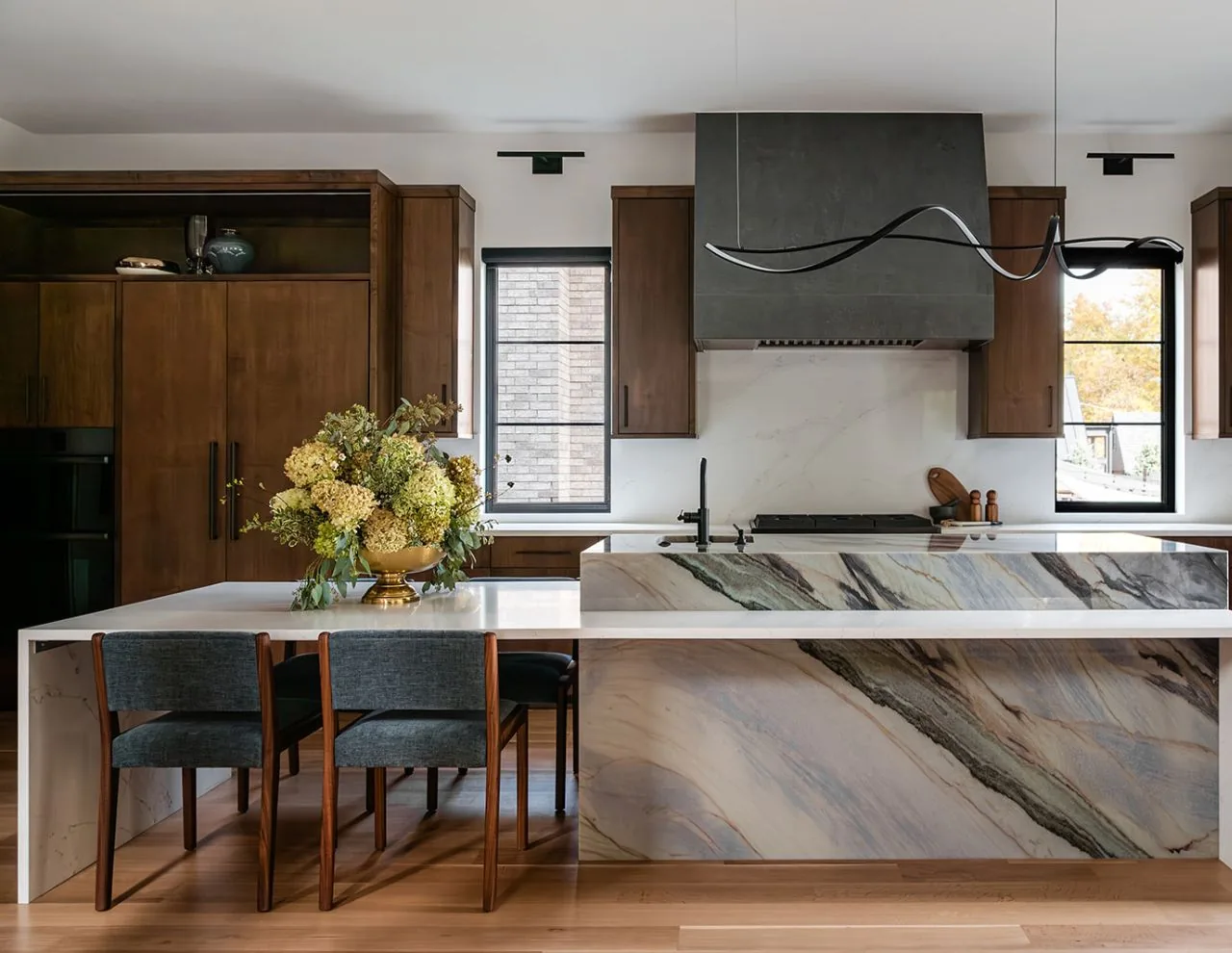 Clarendon Hills Residence kitchen features a marble island, wooden cabinetry, and black window frames.