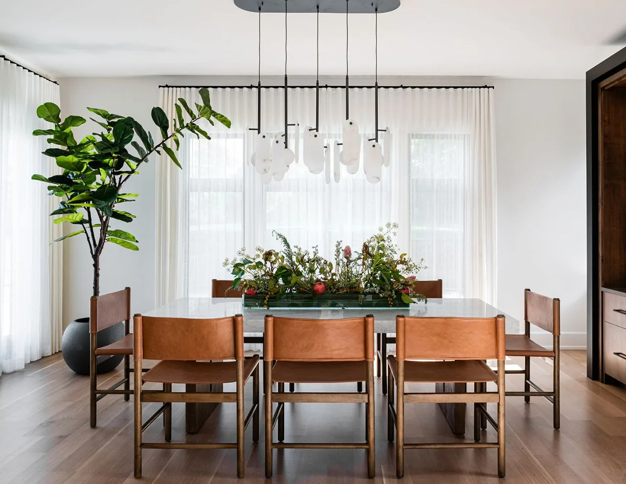 The Clarendon Hills Residence dining area features a marble table, leather seating, and sculptural pendant lighting by Charles Vincent George Architects.