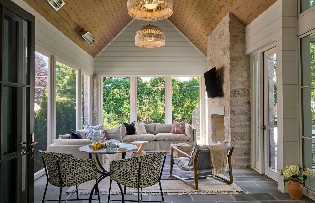 Screened porch with vaulted wood ceiling, stone fireplace, and comfortable seating in a transitional style residence.