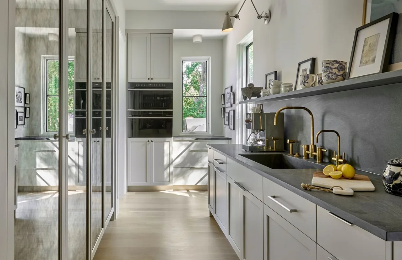 Naperville transitional residence kitchen with gray cabinetry, black countertop, dual brass faucets, and natural light from tall windows.