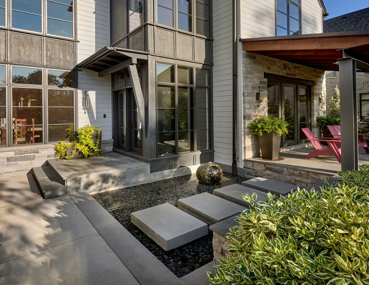 Transitional farmhouse residence exterior with a stone patio, water feature, metal awning, and dormer windows
