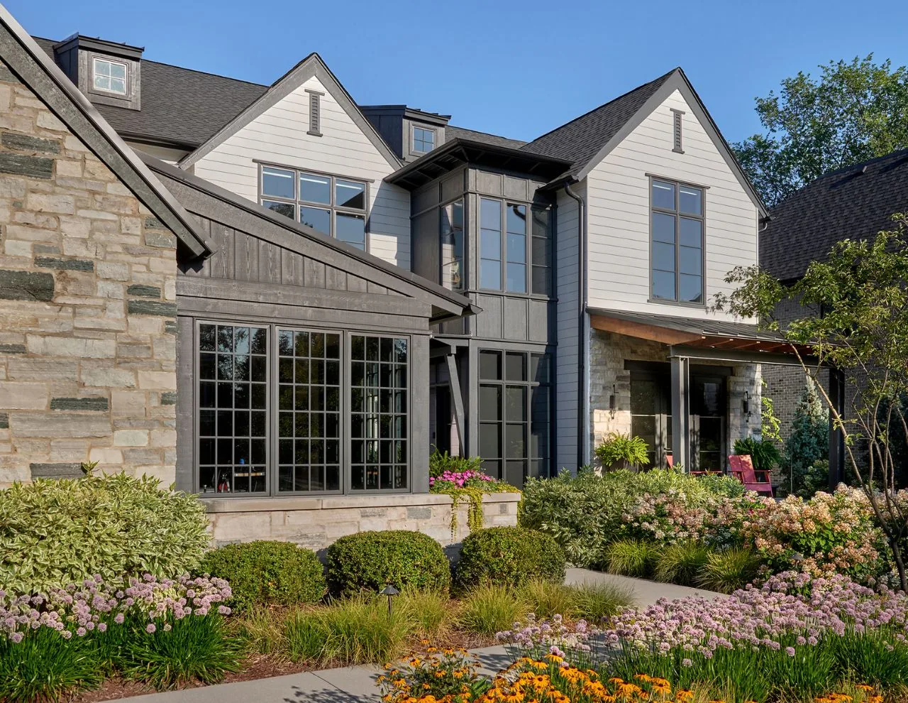 Transitional farmhouse residence with multiple gables, stone and wood siding, and a landscaped garden, designed by Charles Vincent George Architects in Chicago.