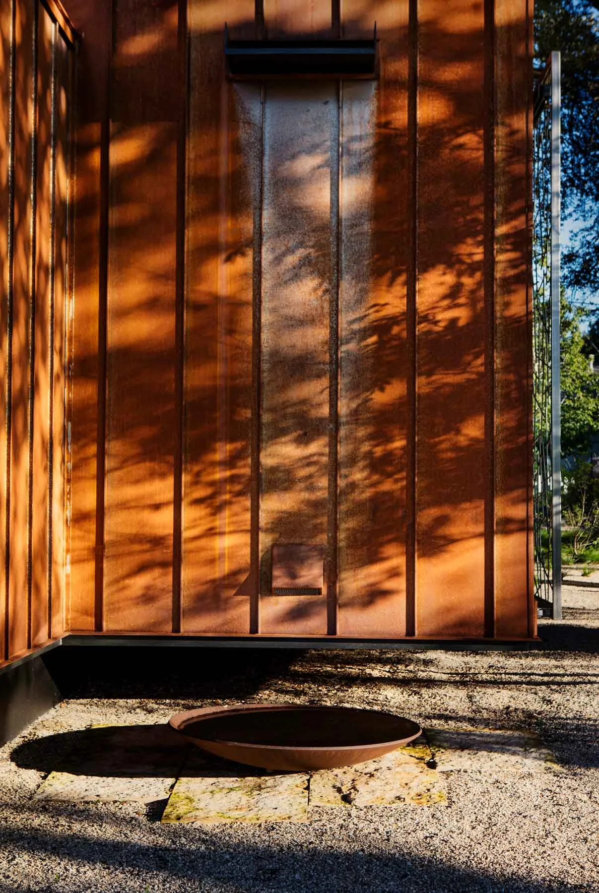 Rust-colored metal siding with vertical grooves on exterior wall, stone paving, and a shallow metal basin in Austin project exterior.