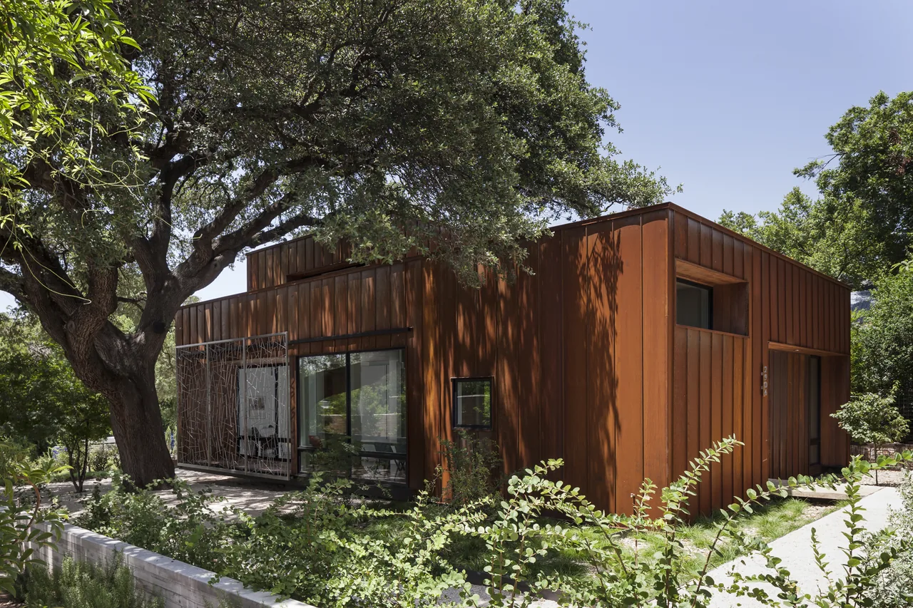 Modern residential building clad in rust-colored metal panels with large windows and landscaping in Austin, TX.